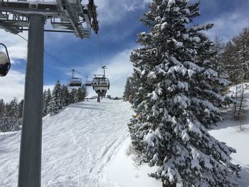 Low angle view of ski lift over snowy field amidst frozen trees against sky