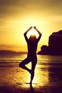 Silhouette woman standing on beach against sky during sunset