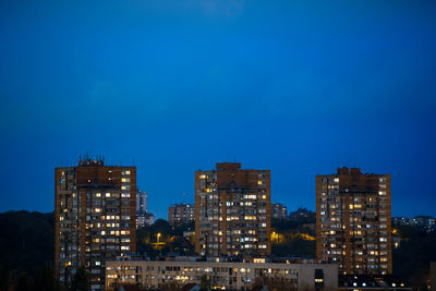 Illuminated buildings against blue sky at dusk