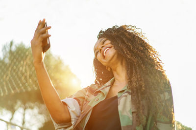 Low angle view of smiling woman using mobile phone against sky
