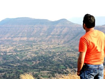 Rear view of man looking at mountains against sky