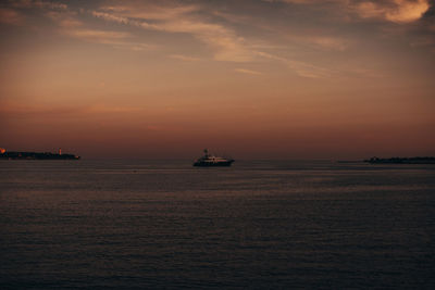 Evening summer sunset with orange sky horizon and boat sailing on the sea