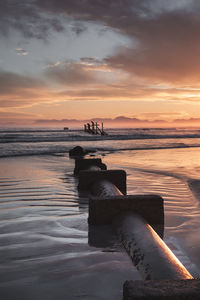 A sewage pipe leads into a beautiful ocean sunset scene 