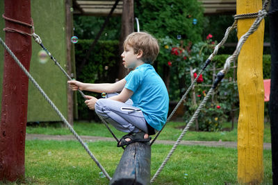 Side view of boy crouching on log at playground