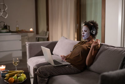 African american lady in sheet mask using laptop