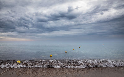 Row of yellow buoys floating on the ocean against stormy sky