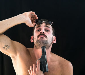 Shirtless man attempting suicide with gun against black background