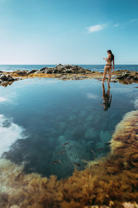 Woman standing on rock by sea against sky