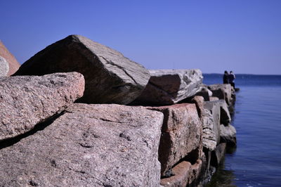 Rocks by sea against clear blue sky