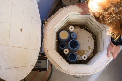 From above of crop faceless female sculptor putting crockery from clay in barrel for drying