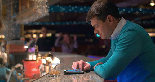 Side view of man using smart phone while sitting on table