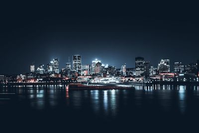 Illuminated buildings by sea against sky at night