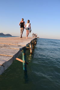 Friends standing in sea against clear sky