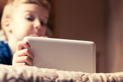 Boy using digital tablet while lying on bed at home