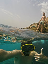 Man wearing gesturing undersea with friend in background