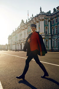 Woman in a black jacket and cap wearing sunglasses walking down the street in square near  building