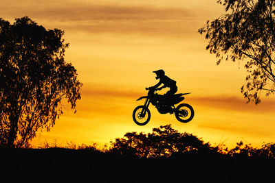 Silhouette man riding bicycle against orange sky