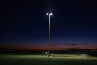 Illuminated street light on field against sky at night