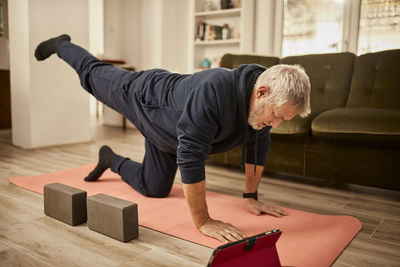 Senior man practicing yoga on exercise mat at home