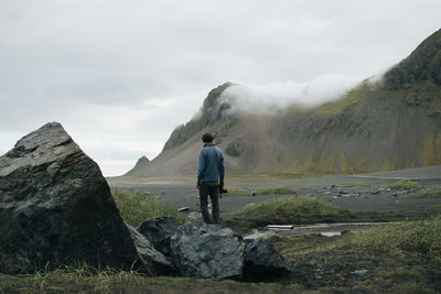 Rear view of man standing on rock against sky