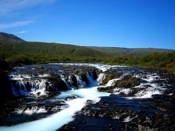 Scenic view of waterfall against clear blue sky