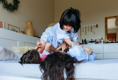 Two children lying on the bed and other child jumping over