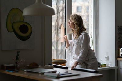 Woman holding coffee cup by window