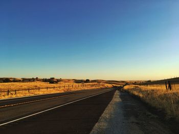 Empty road on field against clear blue sky