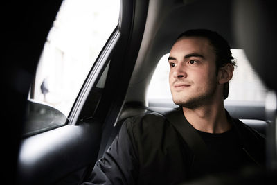 Thoughtful young man looking through window while riding in car at city