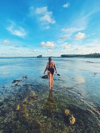 Rear view of woman standing at beach against sky