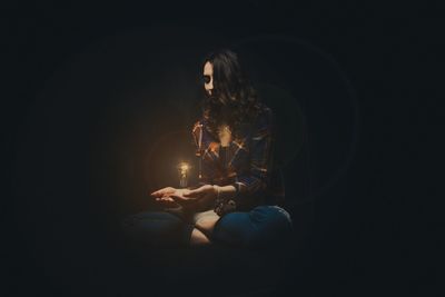 Young woman holding illuminated light bulb against black background