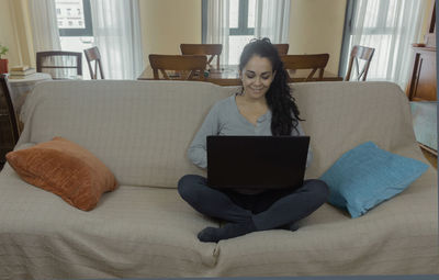 Woman using phone while sitting on sofa at home