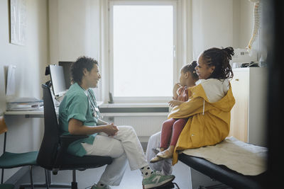 Happy woman carrying daughter discussing with female pediatric in hospital