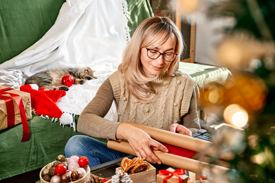 Blond woman wrapping presents in recycled card and decorated it with dried oranges and fir branches.