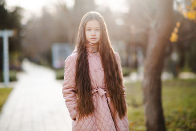 Stylish kid girl 10-12 year old wear jacket with long blonde hair standing in park. autumn season.