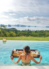 Rear view of woman at swimming pool against sky