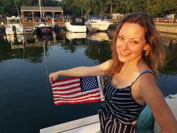 Portrait of smiling mid adult woman holding american flag while standing on boat in lake