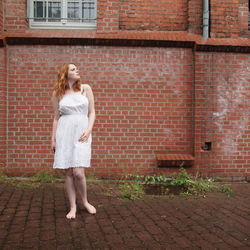 Full length of young woman standing on brick wall