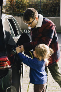 Daughter helping father to plug charger while charging electric car