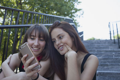 Two young women sitting on a staircase with a smart phone