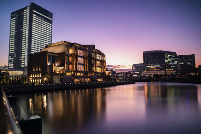 Illuminated buildings by river against sky at night