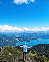 Rear view of man looking at mountains against blue sky