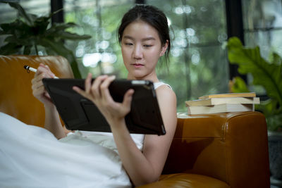 Woman using digital tablet while relaxing on sofa at home