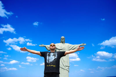 Low angle view of man with arms outstretched standing against christ the redeemer