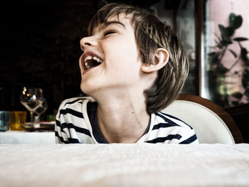 Close-up of boy laughing while sitting on chair by table