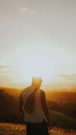 Rear view of man standing on field against sky during sunset