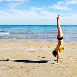 Woman doing handstand at beach against sky