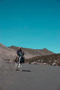 Full length of man riding horse on mountain against clear blue sky