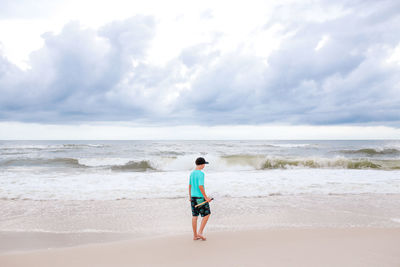 Full length of boy standing at beach against sky