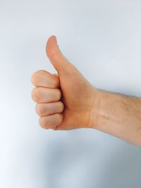 Close-up of hand showing thumbs up against white background